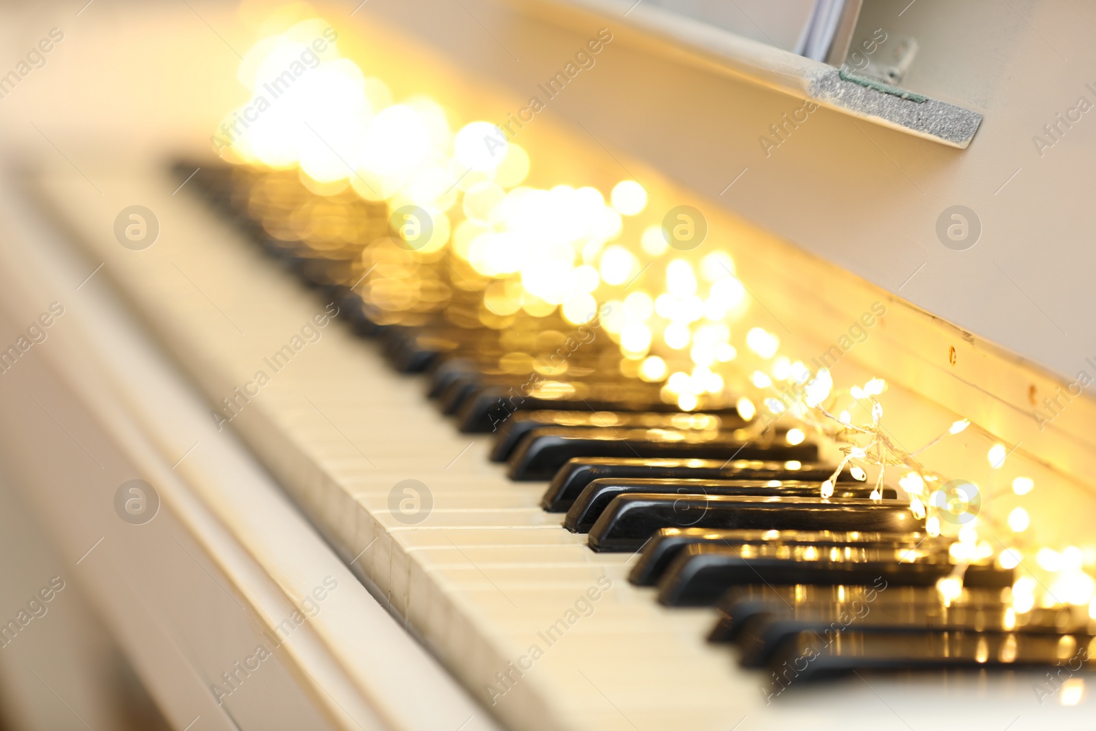 Photo of Glowing fairy lights on piano keys, closeup. Christmas music