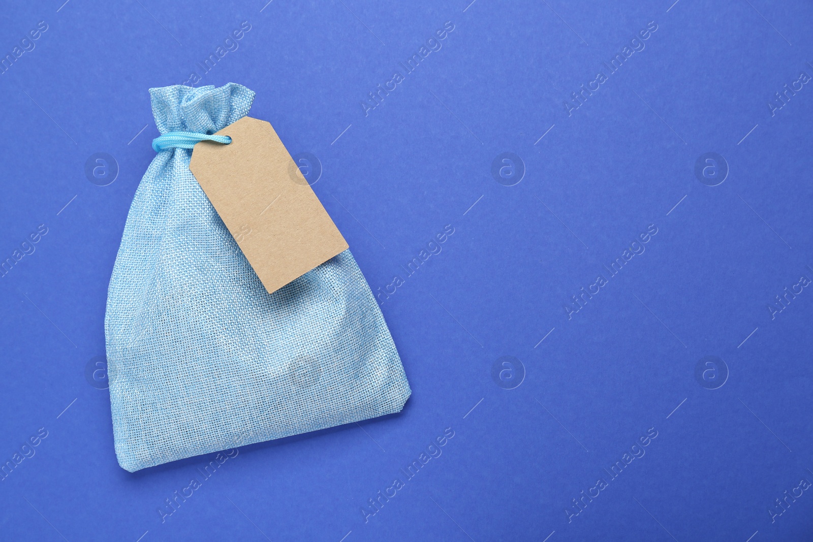 Photo of Color burlap bag with tag on blue background, top view. Space for text