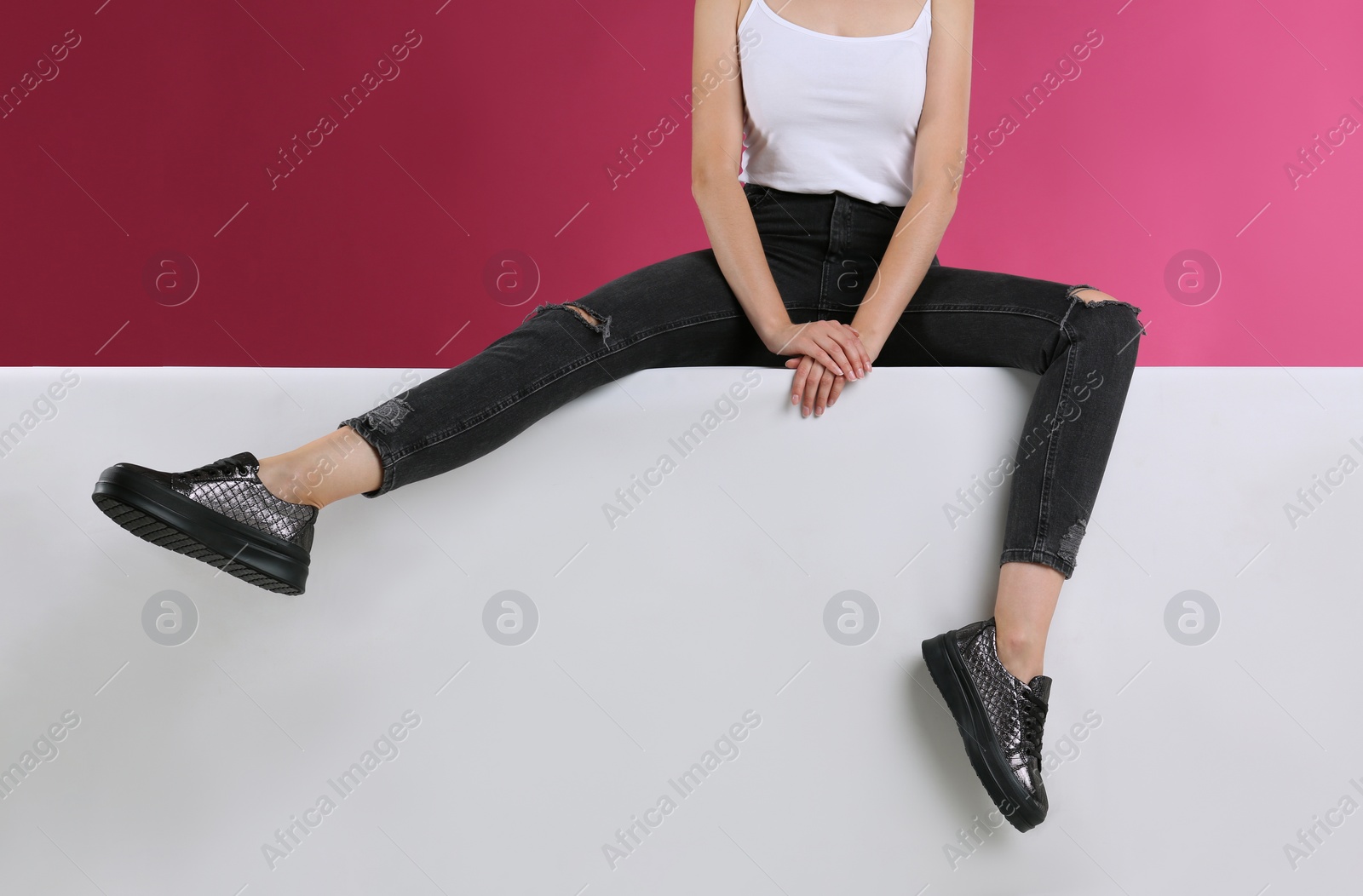 Photo of Woman in stylish shoes sitting on color background, closeup