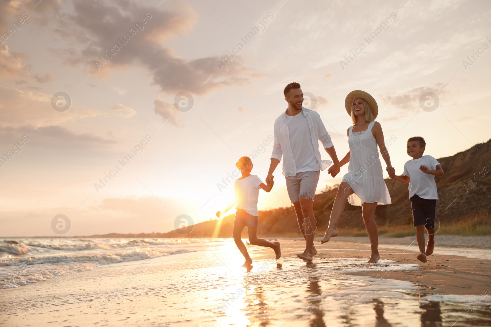 Photo of Happy family running on sandy beach near sea at sunset