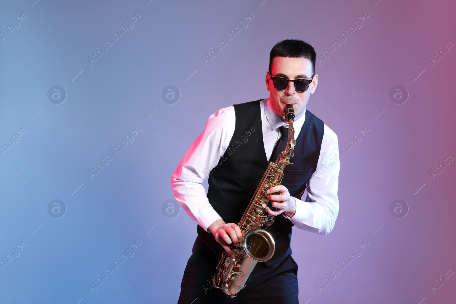 Photo of Young man in elegant outfit playing saxophone on color background. Space for text