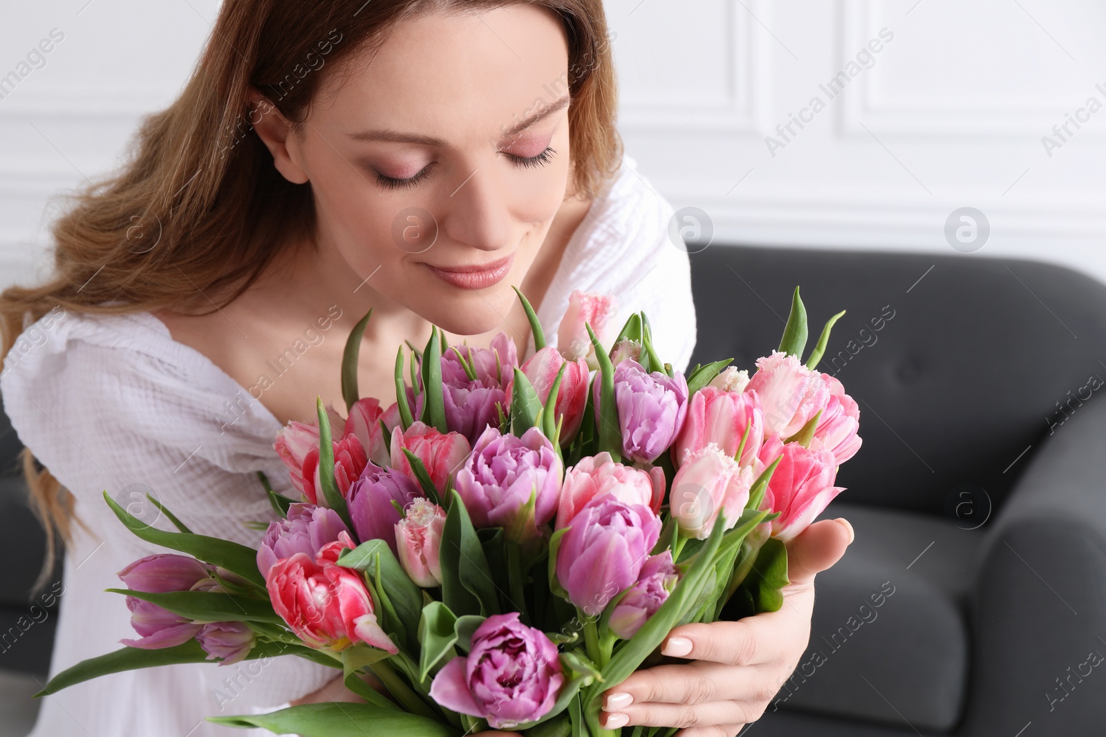 Photo of Young woman with bouquet of beautiful tulips indoors