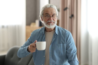 Portrait of happy grandpa with glasses and cup of drink indoors