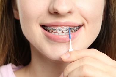 Photo of Smiling woman with dental braces cleaning teeth using interdental brush, closeup
