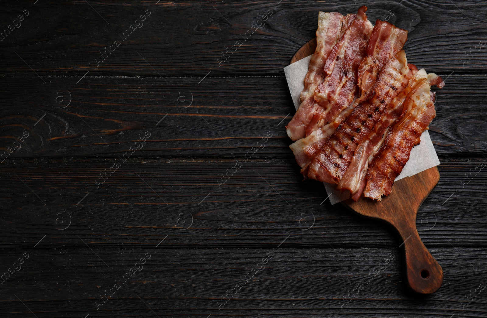 Photo of Slices of tasty fried bacon on black wooden table, top view. Space for text