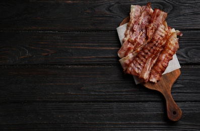 Slices of tasty fried bacon on black wooden table, top view. Space for text