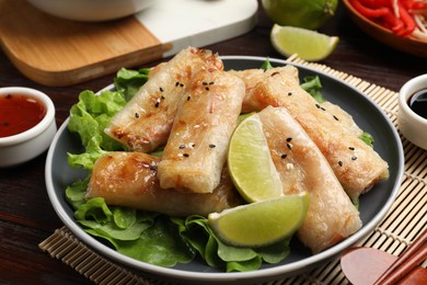 Photo of Tasty fried spring rolls, lettuce and sauce on wooden table, closeup