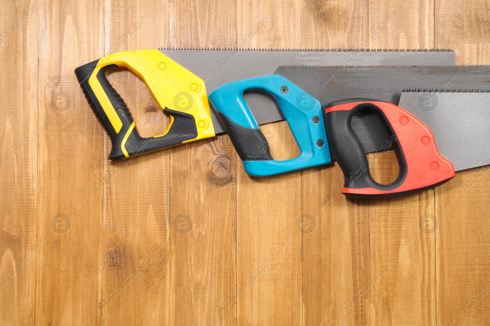 Photo of Saws with colorful handles on wooden background, flat lay. Space for text