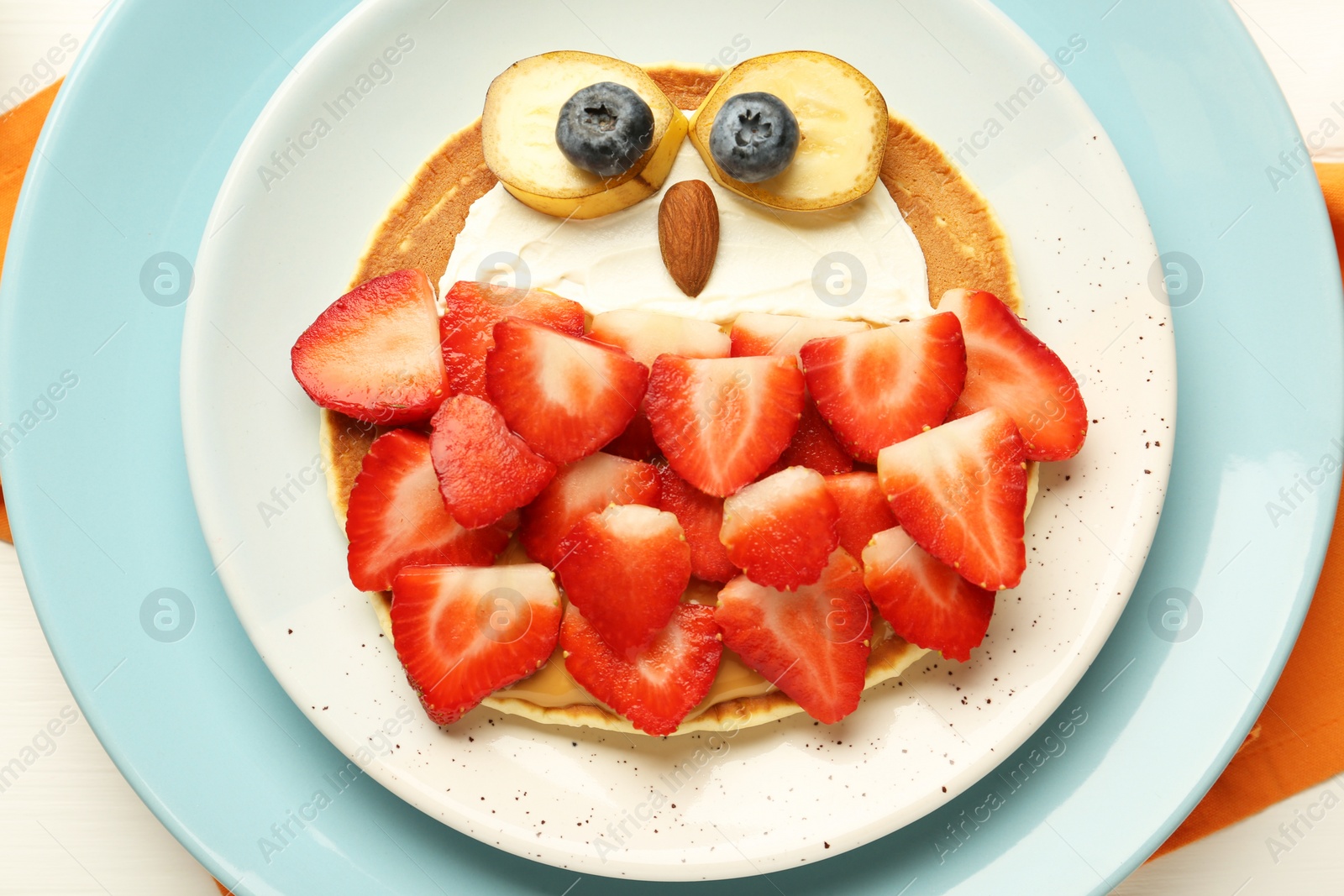 Photo of Creative serving for kids. Plate with cute owl made of pancakes, strawberries, cream, banana and almond on white wooden table, top view