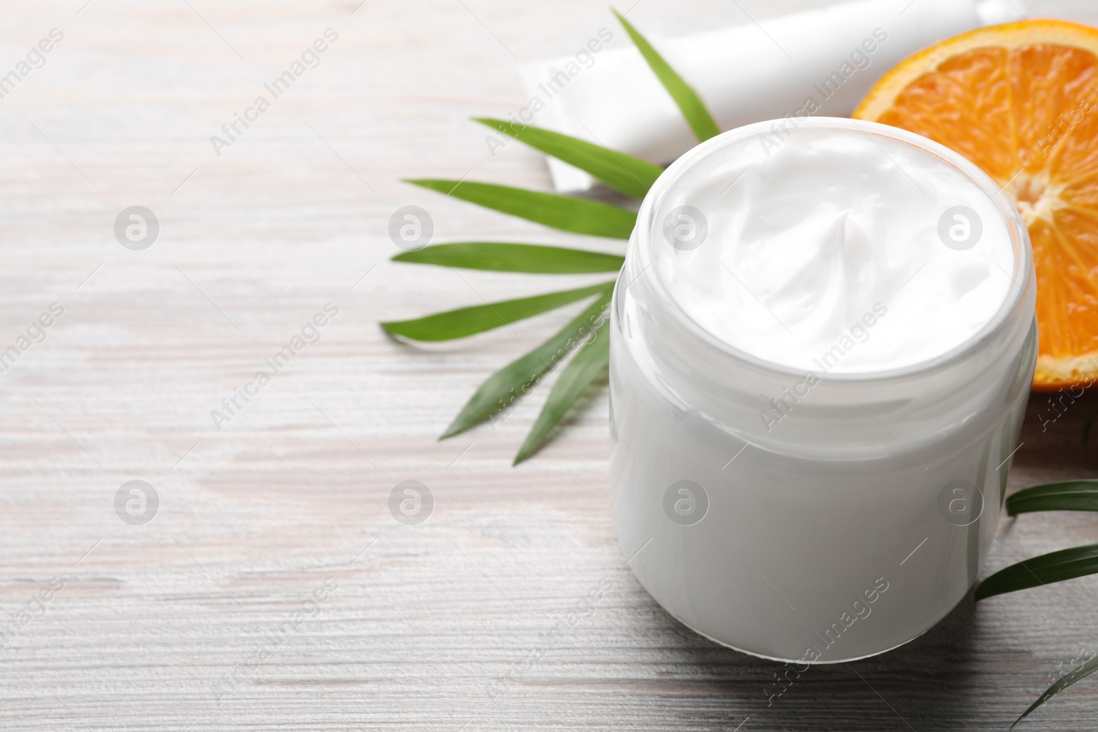 Photo of Jar of hand cream, orange and green leaves on white wooden table, space for text