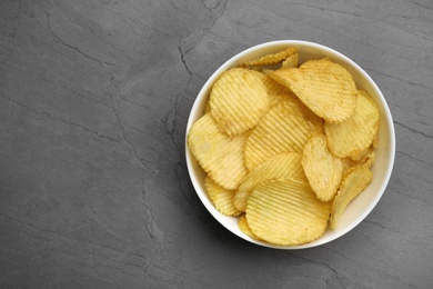 Bowl of potato chips on grey table, top view. Space for text