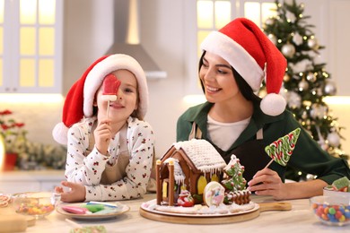 Photo of Mother and daughter having fun while decorating gingerbread house at table indoors