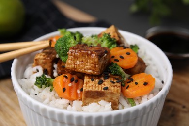 Bowl of rice with fried tofu, broccoli and carrots on wooden board, closeup