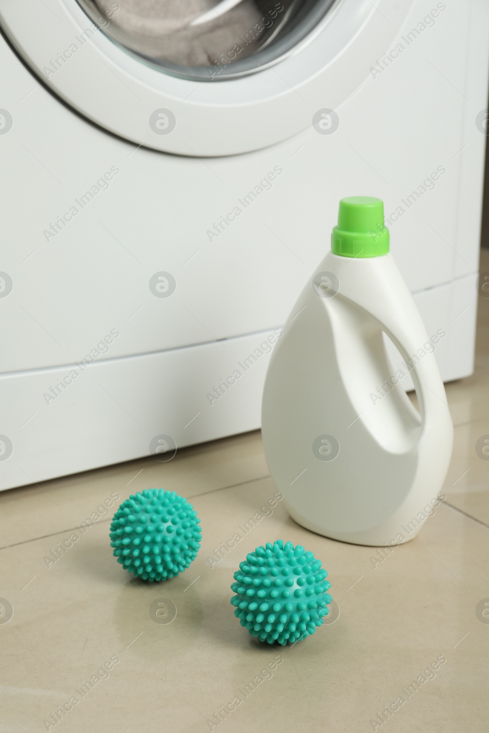 Photo of Laundry detergent and dryer balls near washing machine on floor