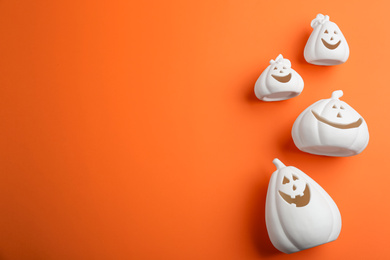 Image of White pumpkin shaped candle holders and space for text on orange background, flat lay. Halloween decoration