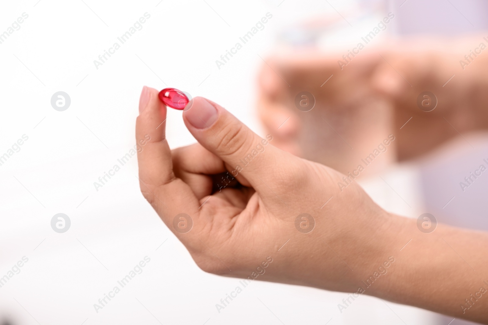 Photo of Woman holding pill and glass of water on blurred background, closeup. Space for text