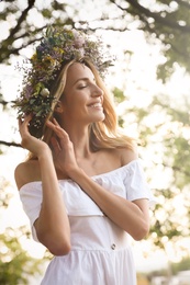 Young woman wearing wreath made of beautiful flowers outdoors on sunny day