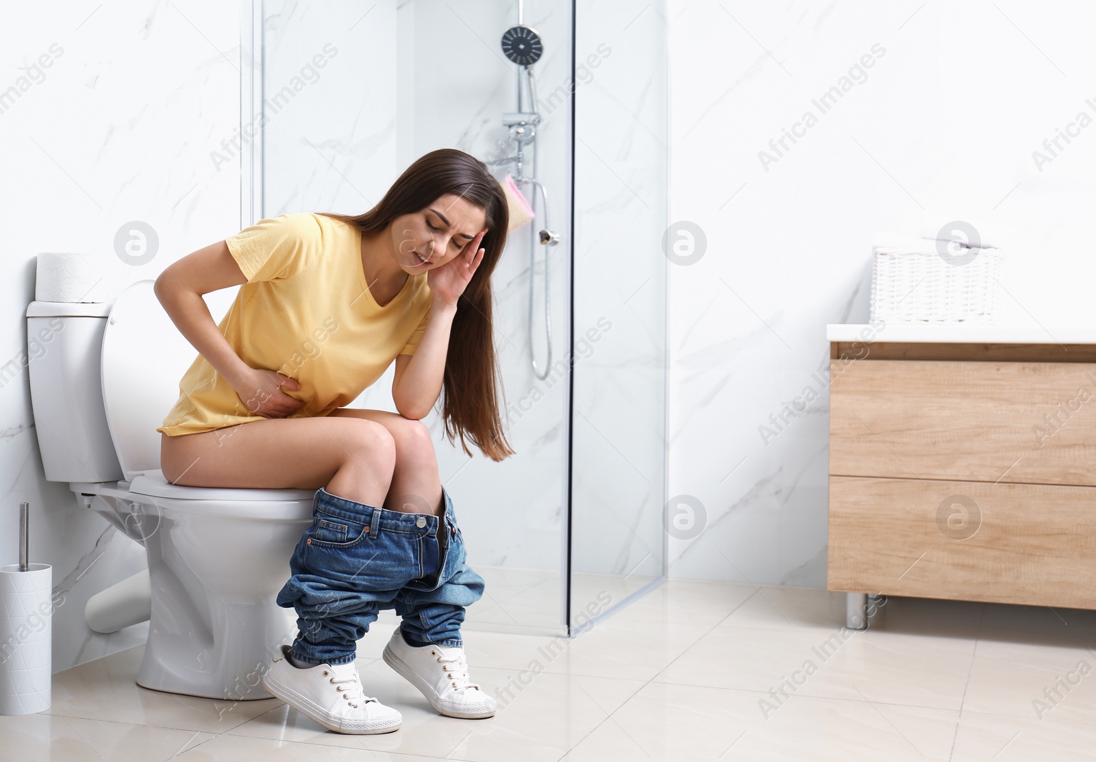 Photo of Woman with stomach ache sitting on toilet bowl in bathroom