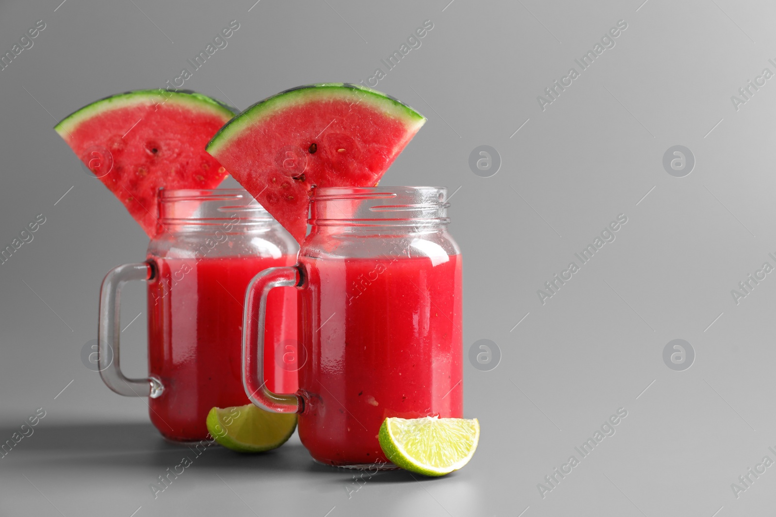 Photo of Tasty summer watermelon drink with lime in glass mason jars on grey background. Space for text