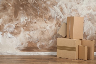 Photo of Pile of cardboard boxes near brown wall indoors. Space for text