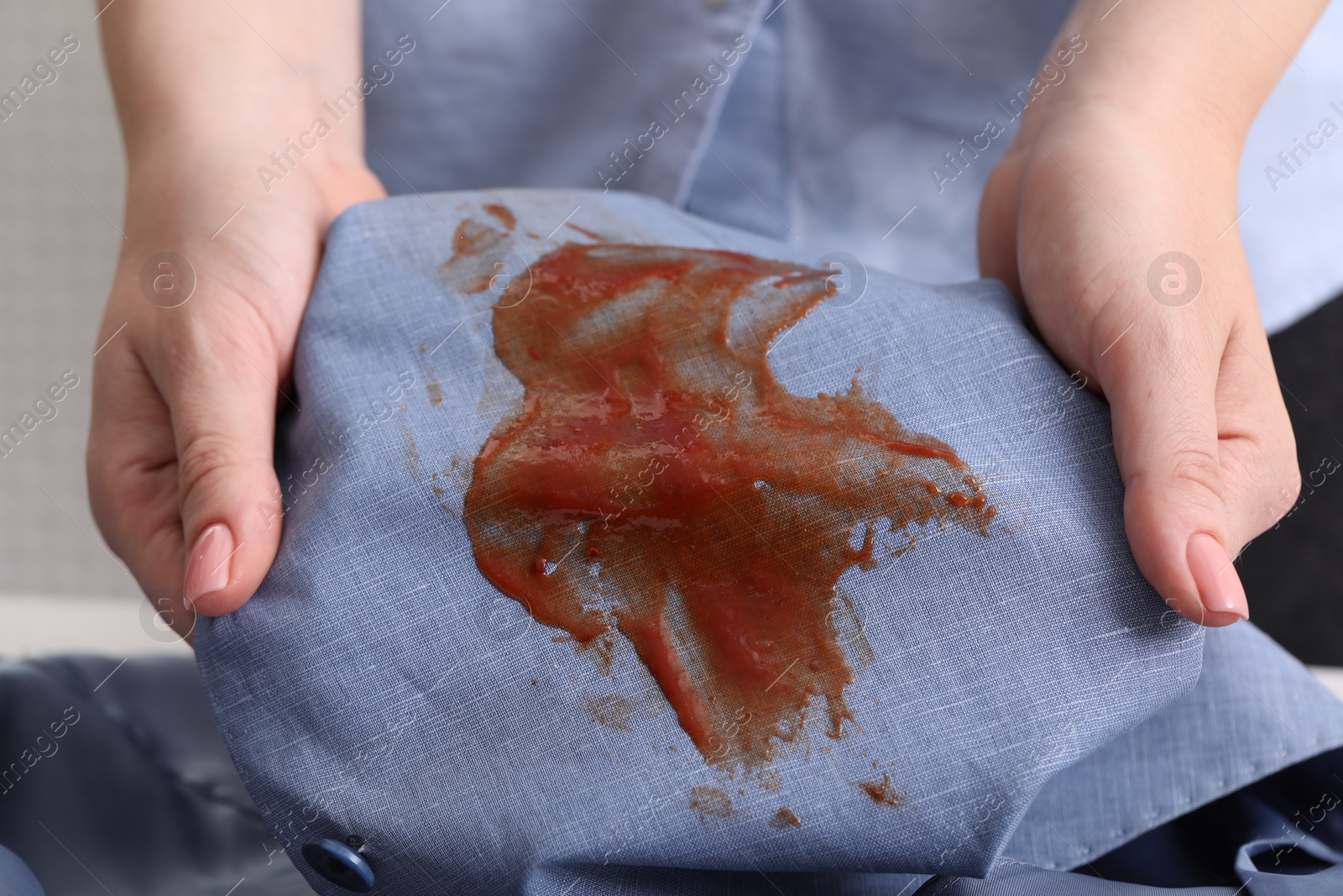 Photo of Woman holding shirt with stain of sauce on blurred background, closeup