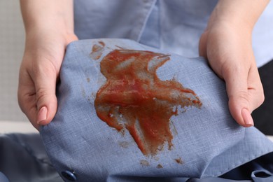 Woman holding shirt with stain of sauce on blurred background, closeup