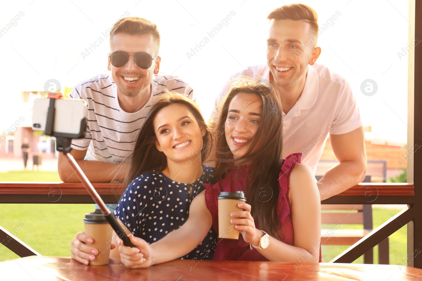 Photo of Group of young people taking selfie with monopod in gazebo on sunny day