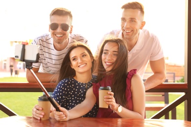 Group of young people taking selfie with monopod in gazebo on sunny day