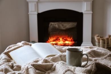 Photo of Cup of hot tea and book near fireplace at home. Cozy atmosphere