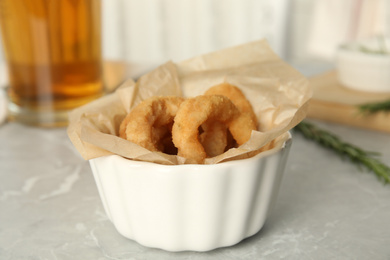 Photo of Delicious crunchy fried onion rings on grey marble table