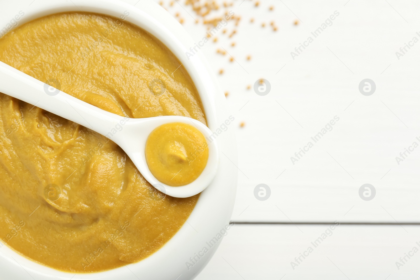 Photo of Bowl and spoon with tasty mustard sauce on white wooden table, top view. Space for text