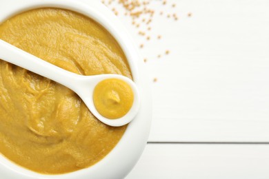 Photo of Bowl and spoon with tasty mustard sauce on white wooden table, top view. Space for text