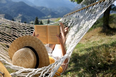 Photo of Young woman reading book in hammock outdoors on sunny day