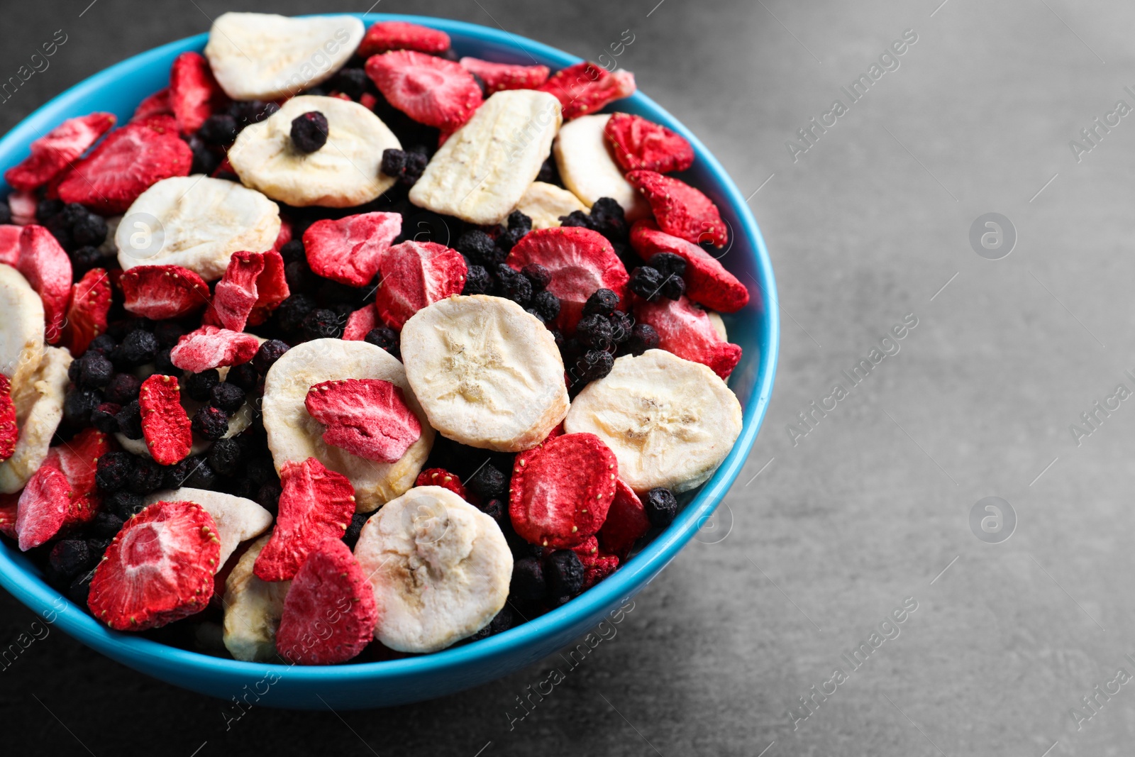 Photo of Bowl of dried fruits on grey table, closeup. Space for text