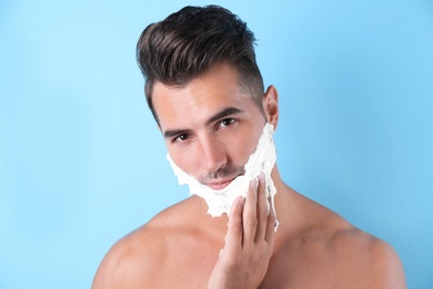 Photo of Handsome young man applying shaving foam on color background