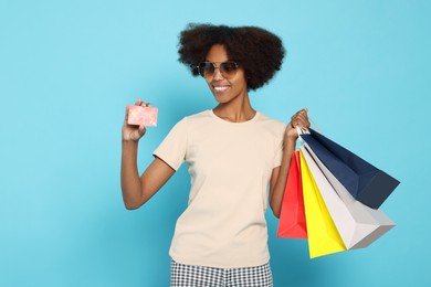 Photo of Happy African American woman in sunglasses with shopping bags and credit card on light blue background