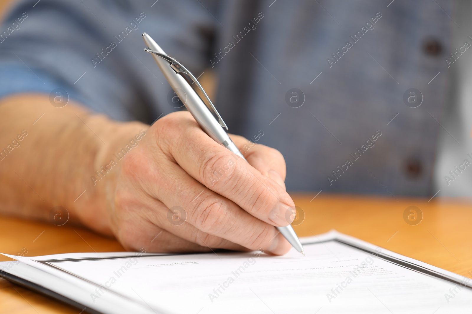 Photo of Senior man signing Last Will and Testament at wooden table, closeup