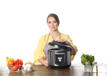 Young woman preparing food with modern multi cooker at table against white background