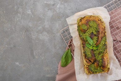 Photo of Freshly baked pesto bread with basil on grey table, top view. Space for text