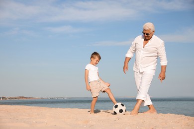 Cute little boy and grandfather playing with soccer ball on sea beach