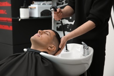Photo of Professional barber washing client's hair at sink in salon, closeup