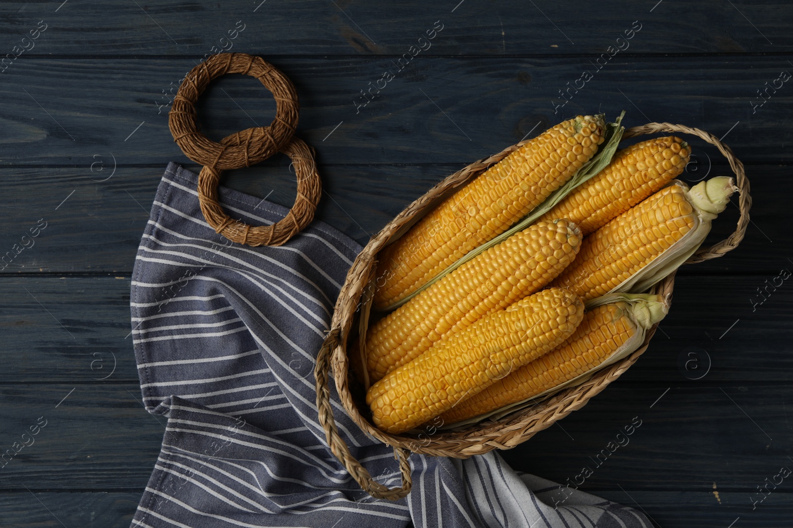 Photo of Corn cobs in basket on dark wooden table, flat lay