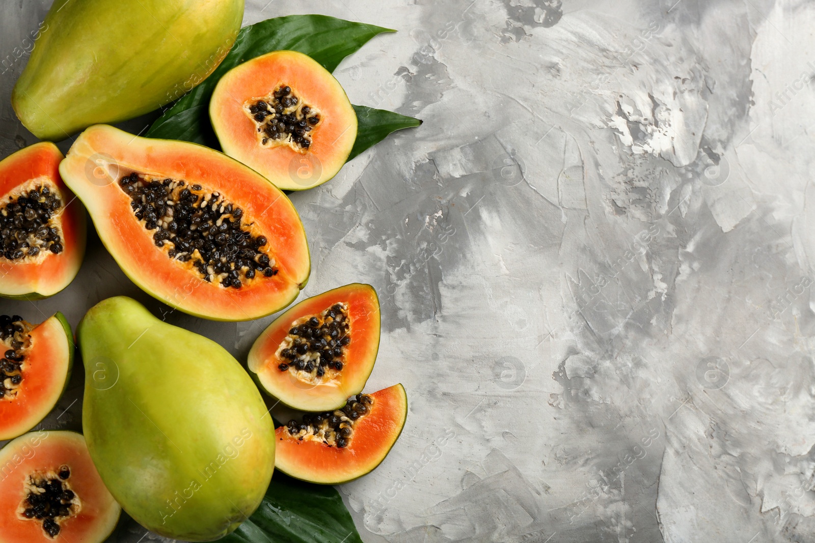 Photo of Fresh ripe papaya fruits with green leaves on grey table, flat lay. Space for text