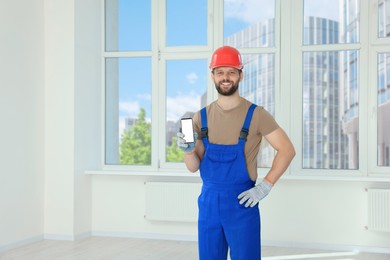 Photo of Professional repairman in uniform with phone indoors, space for text