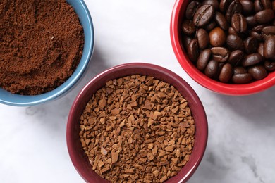 Photo of Instant, ground coffee and roasted beans in cups on white marble table, flat lay