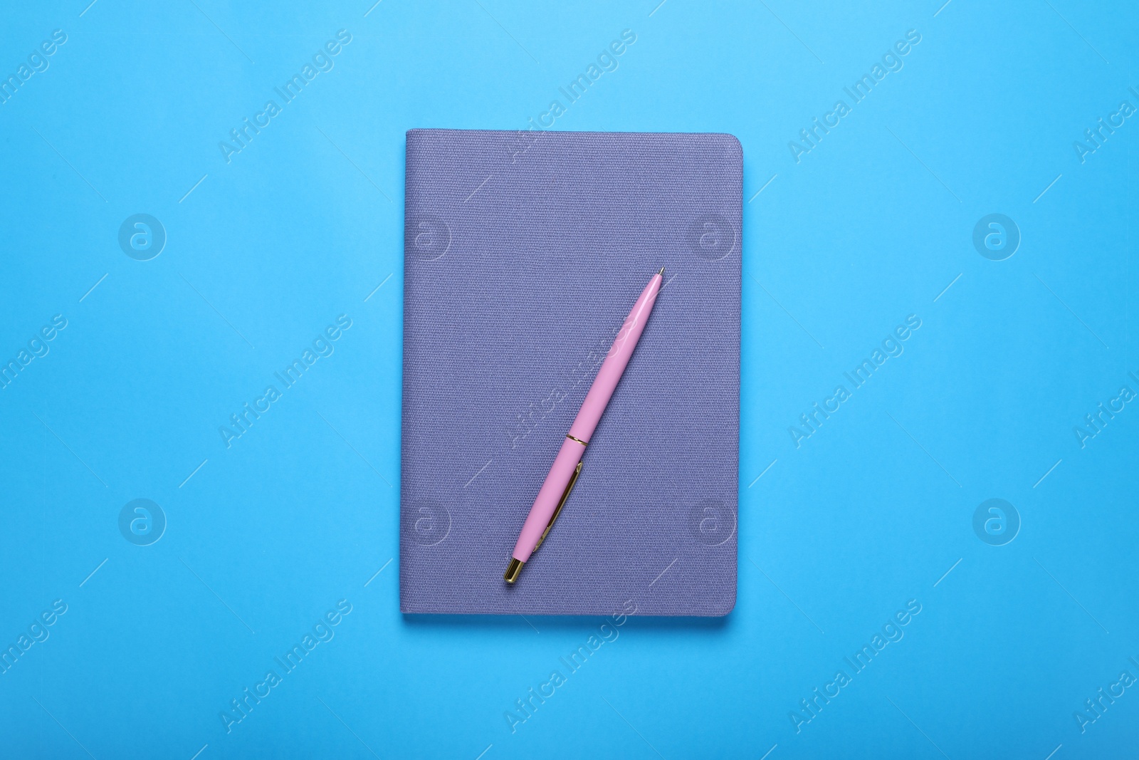 Photo of Closed notebook and pen on light blue background, top view