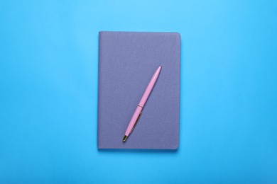 Closed notebook and pen on light blue background, top view