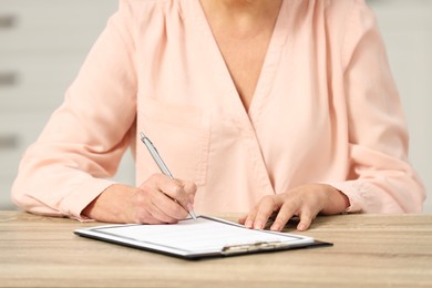 Photo of Senior woman signing Last Will and Testament at wooden table indoors, closeup