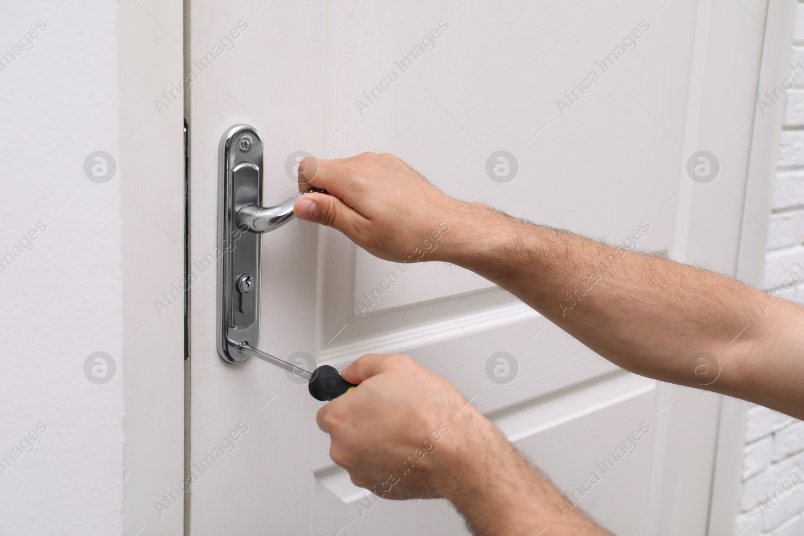 Photo of Handyman with screwdriver repairing door lock indoors, closeup