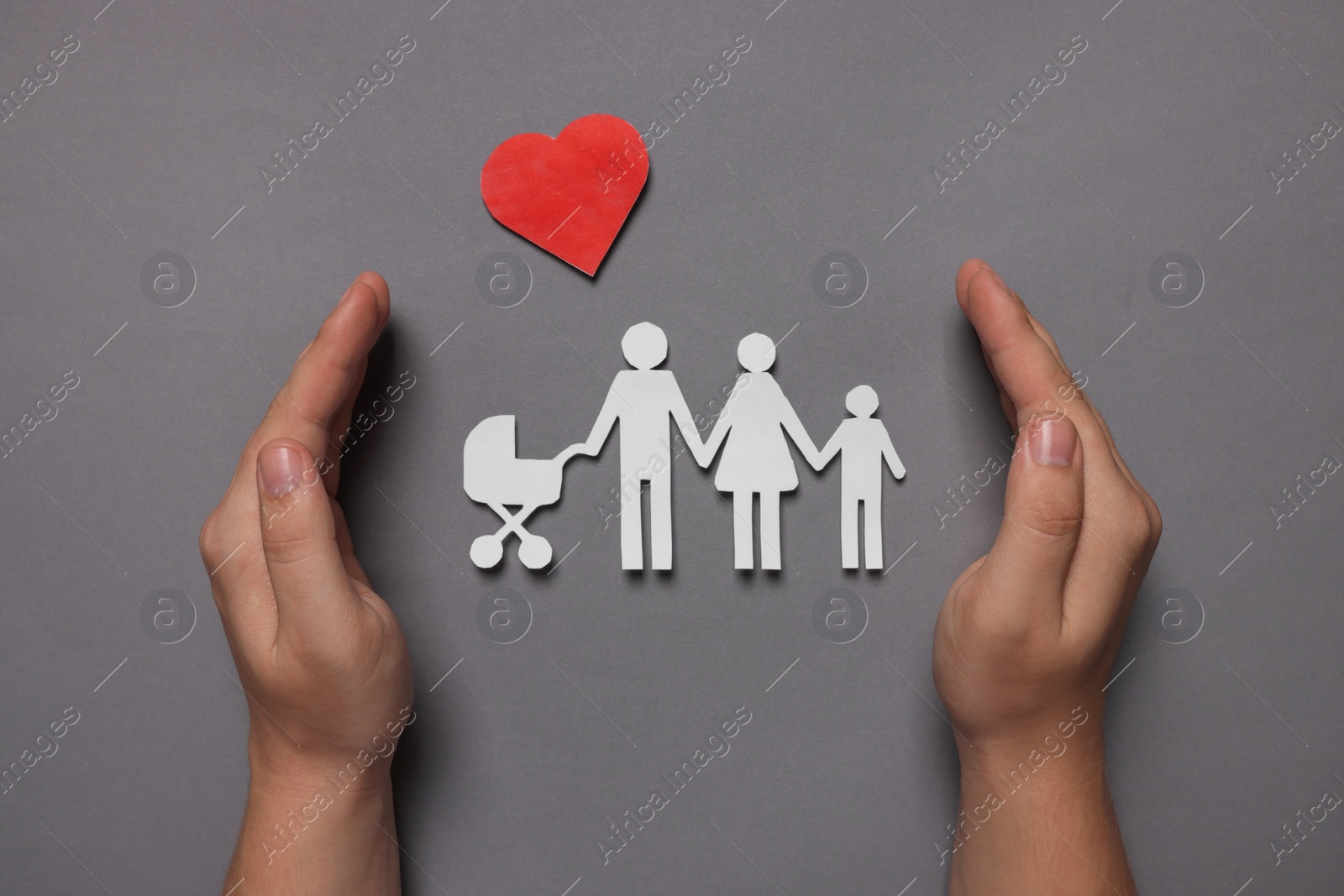 Photo of Man protecting paper family figures and red heart on grey background, top view. Insurance concept